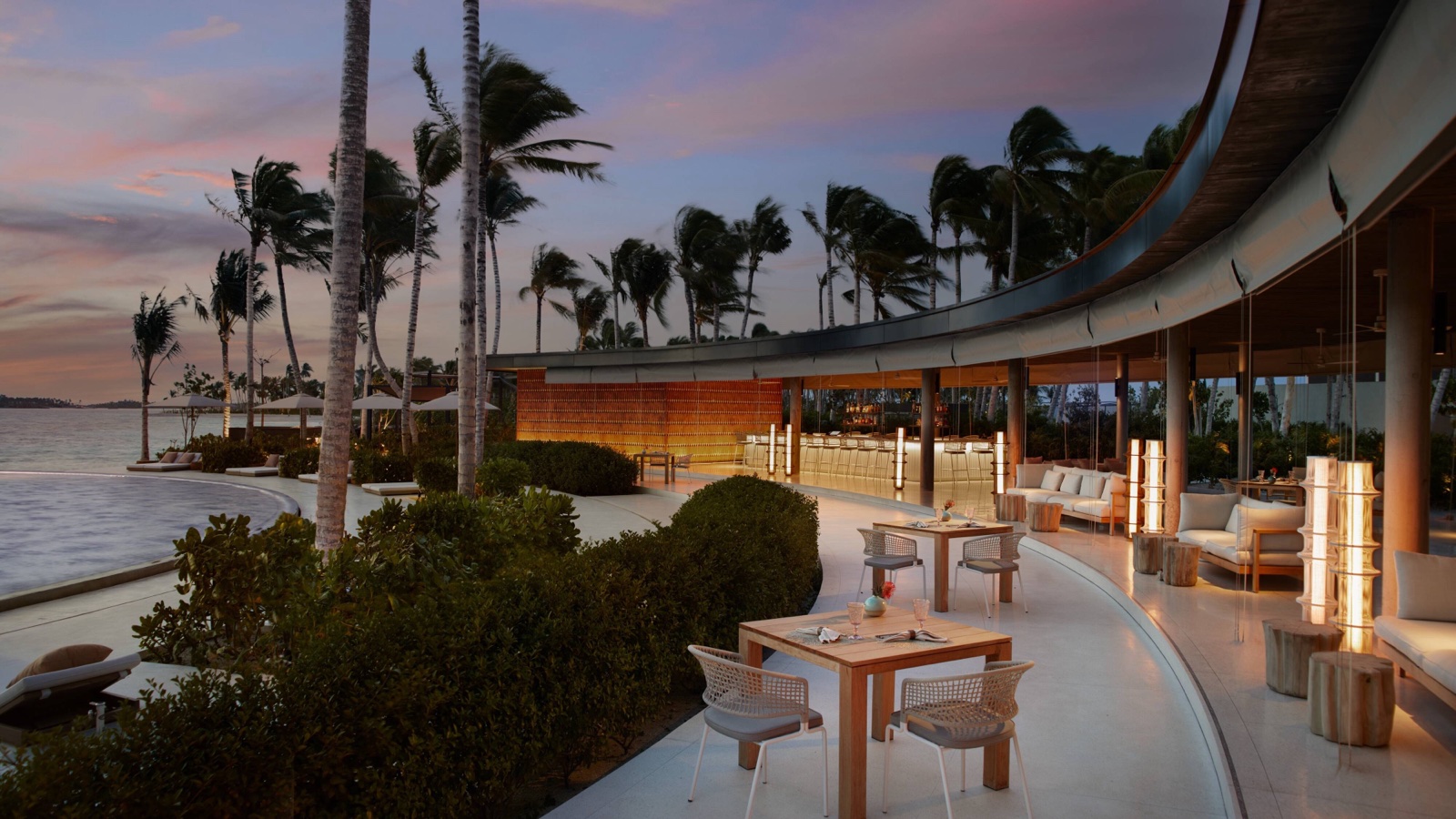 Restaurante de playa con arquitectura curva, palmeras al ocaso e infinity pool en las Maldivas